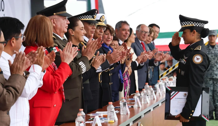 Ficha de imagen Texto alternativo (alt): Presidenta Claudia Sheinbaum y funcionarios aplauden a una elemento de la Guardia Nacional que recibe un reconocimiento durante el 7° aniversario de la institución.