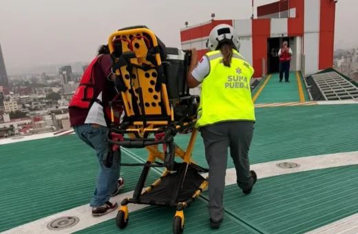 Personal de SUMA Puebla traslada camilla de emergencia en helipuerto sobre azotea, con vista de la ciudad al fondo.