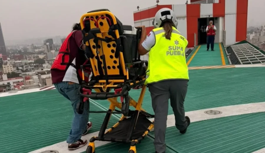 Personal de SUMA Puebla traslada camilla de emergencia en helipuerto sobre azotea, con vista de la ciudad al fondo.